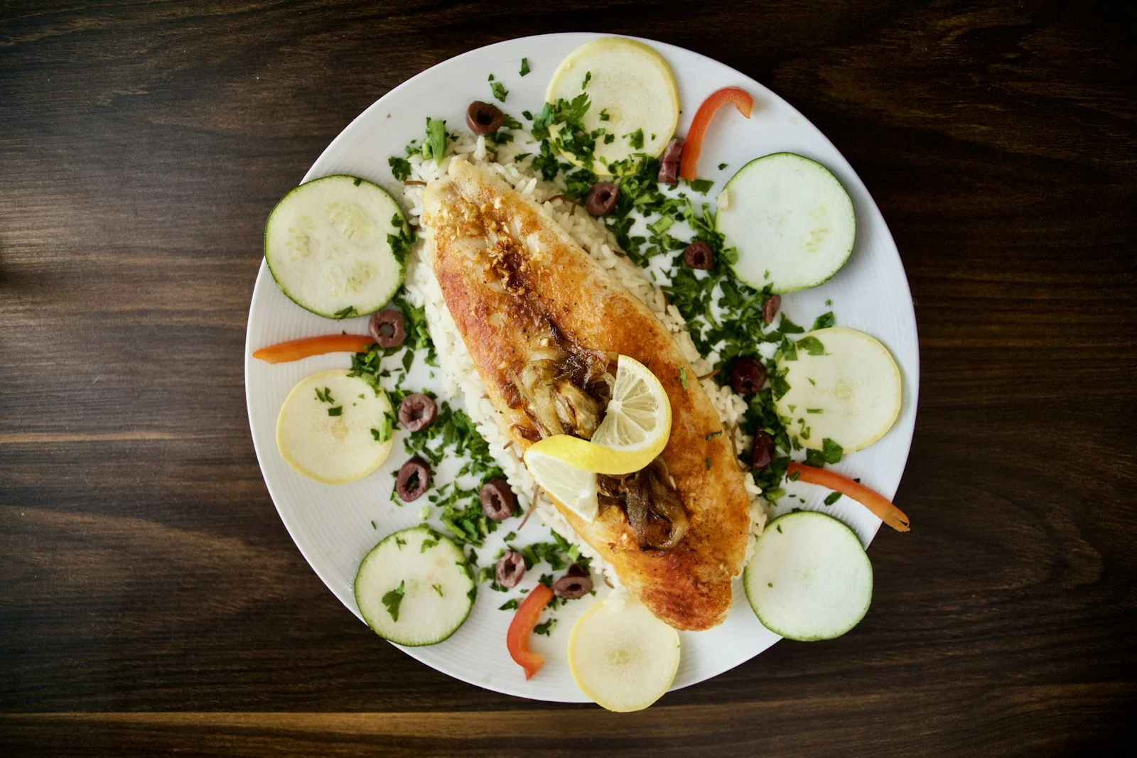 Plate of baked fish with cucumber, tomatoes and greens