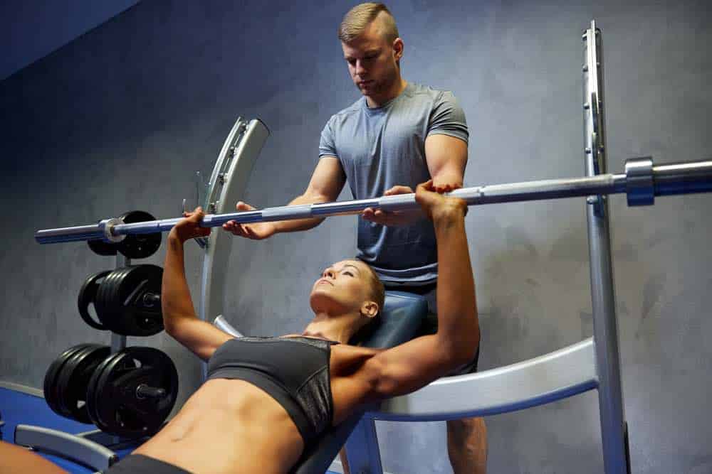 Woman doing a barbell bench press on an Olympic weight bench with a spotter