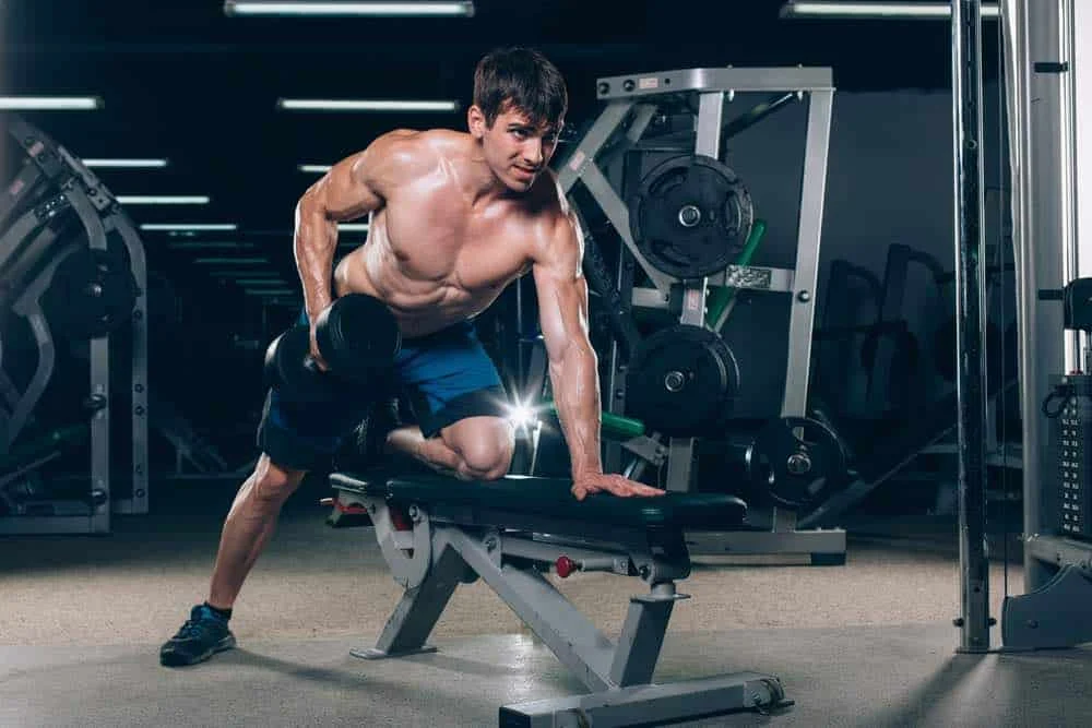 Muscular man flexing while holding dumbbells in the gym